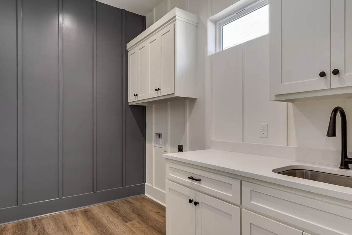 Interior view of a laundry room with white cabinets, sink, dark faucet, and dark paneled wall.