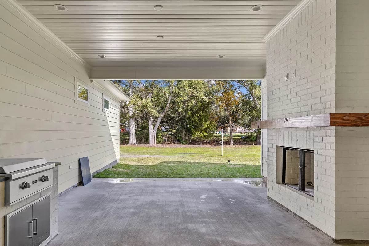 Covered patio with built-in grill and white brick fireplace with wooden mantle. Outdoor living space.