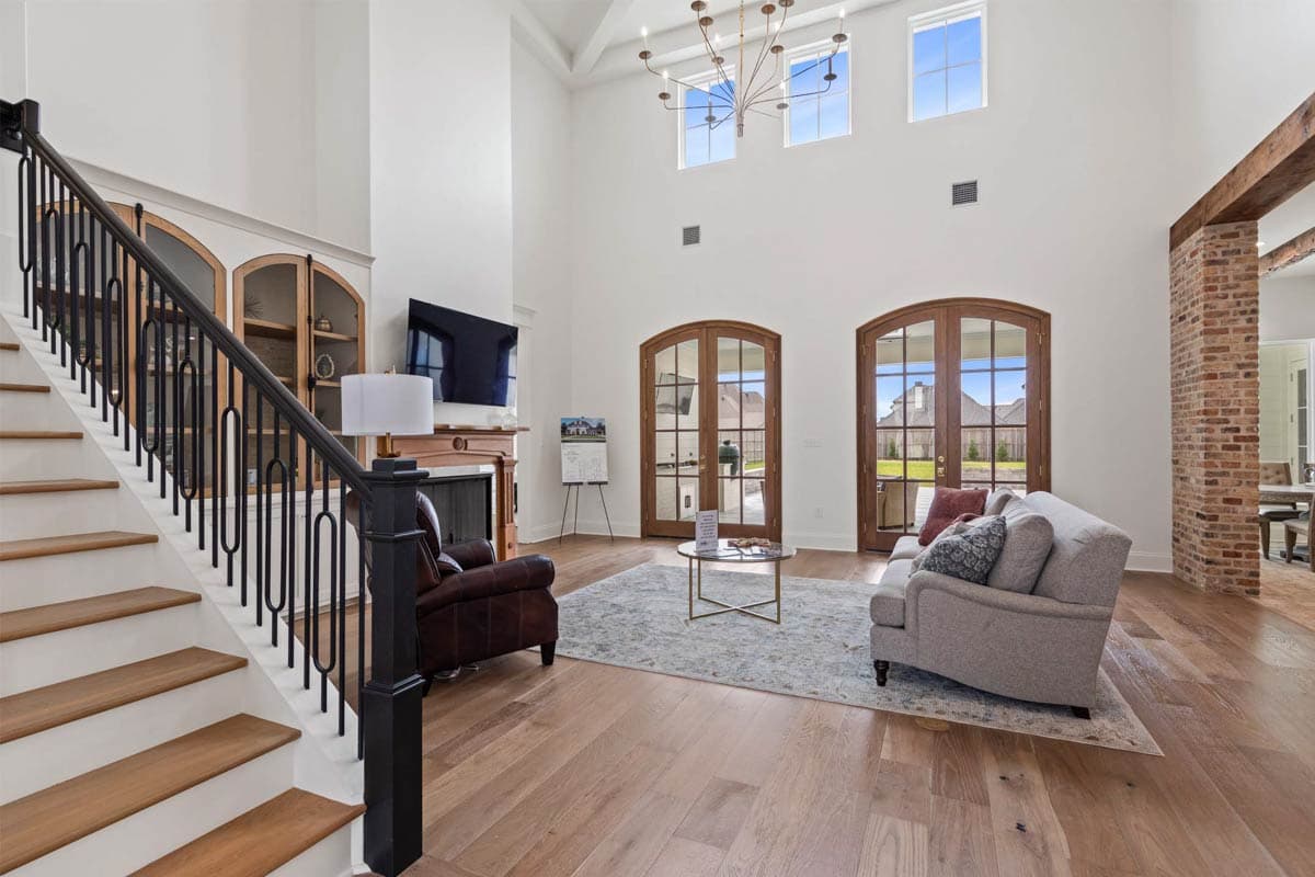 Interior rendering of a great room with a vaulted ceiling, staircase, fireplace, and French doors leading outside.