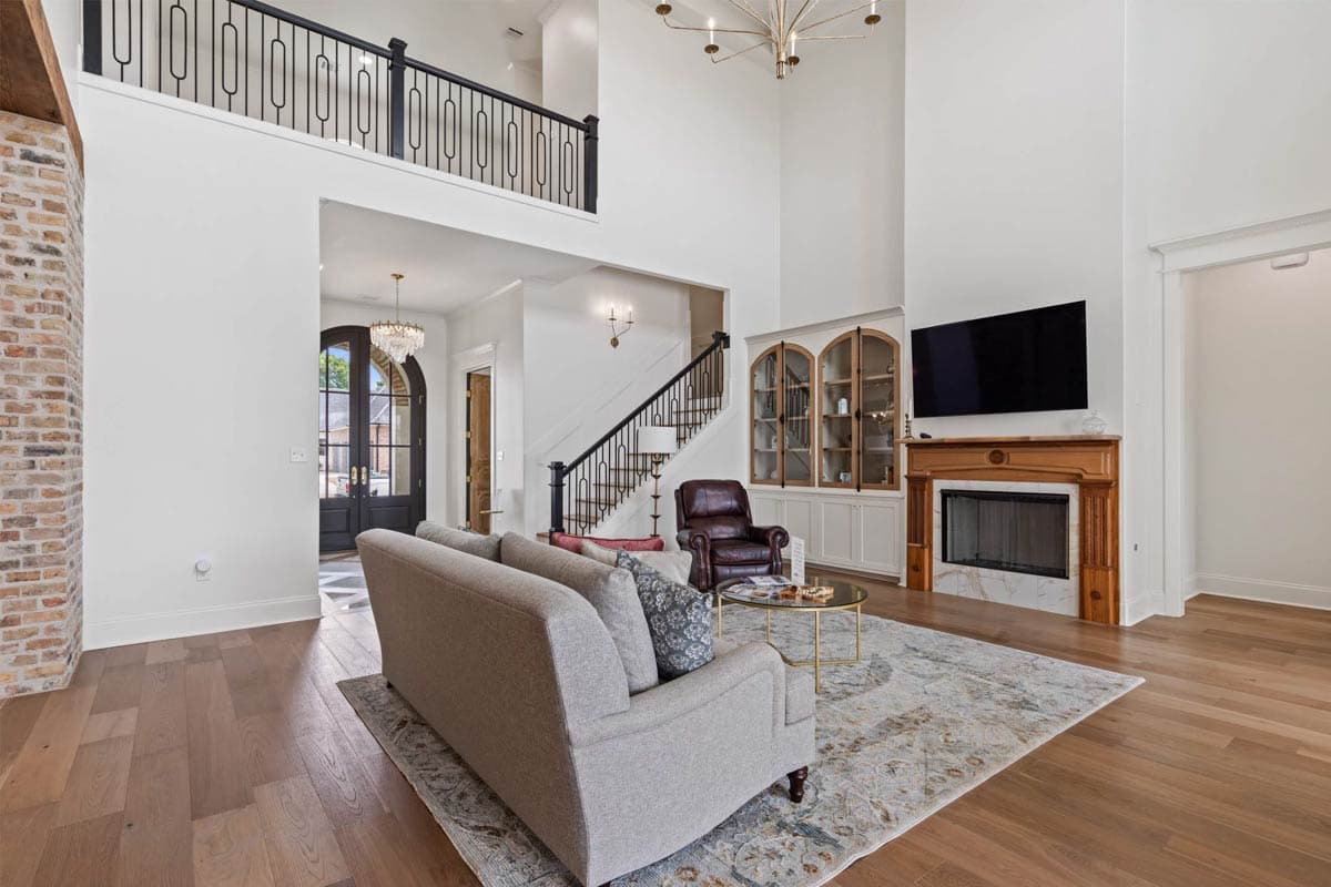 Interior view of great room with two-story ceiling, fireplace, built-in cabinets, staircase, and balcony overlooking entryway.