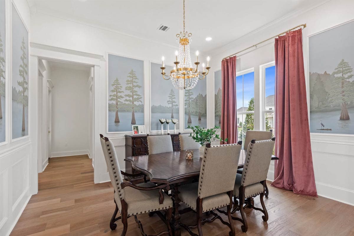 Dining room with a dark wood table, upholstered chairs, crystal chandelier, and scenic mural wallpaper.