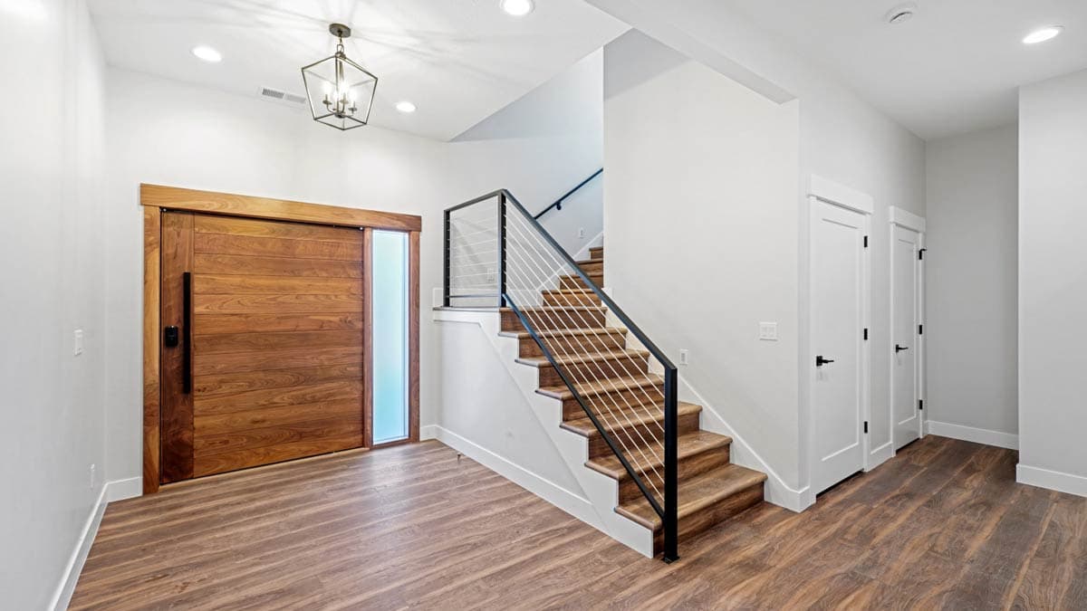 Interior view of a house with a large wooden sliding door, a floating staircase with cable railings, and white doors.
