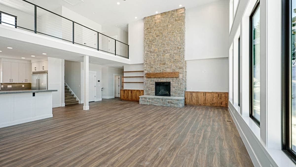 Great room with vaulted ceiling, stone fireplace, kitchen island, open loft with cable railing, and large windows.