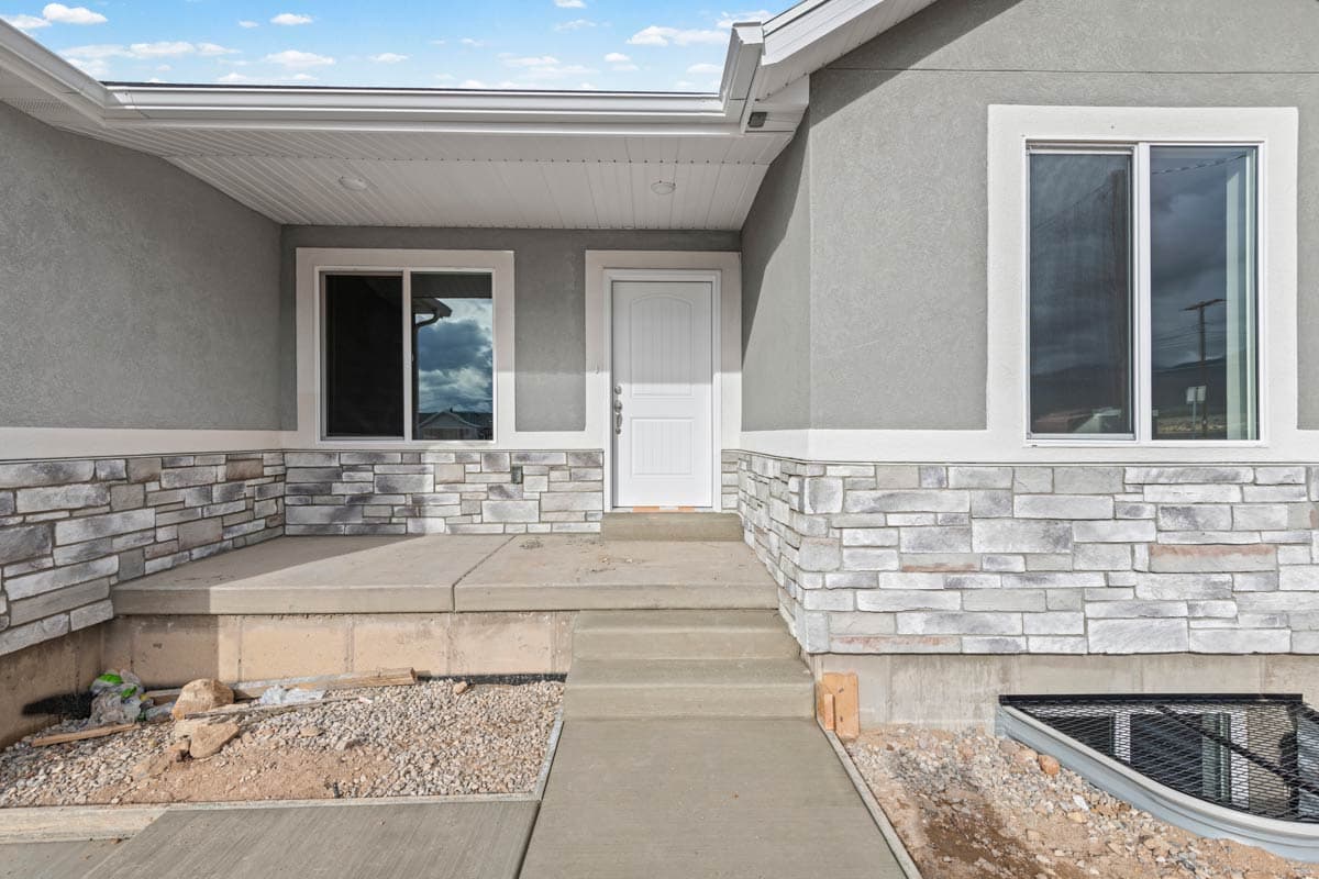House plan exterior with stucco, stone veneer accents, covered porch, and multiple windows.