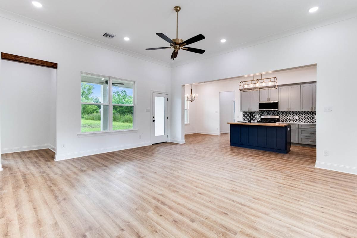 Open-concept living area with vaulted ceiling, large windows, and view of a kitchen with gray cabinets and navy island.