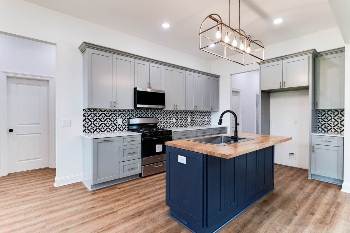 Kitchen with gray cabinets, black and white patterned backsplash, large island with sink, and wood-look flooring.