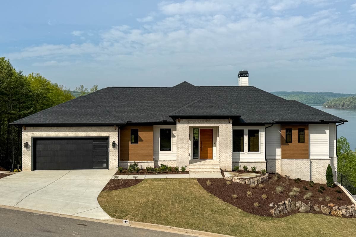 House plan exterior featuring a single-story modern design. Includes a two-car garage, brick facade, wood accents, and a low-sloped roof.