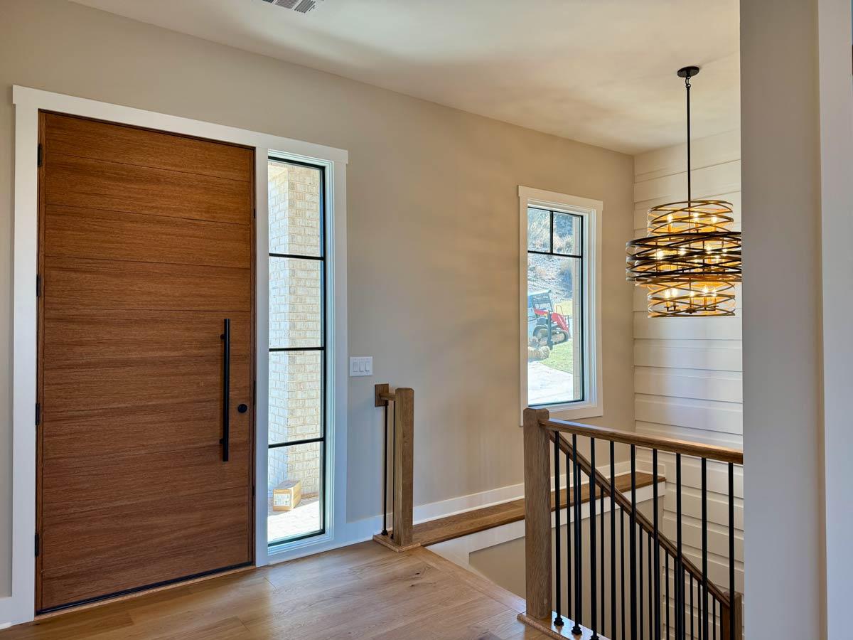 Modern entry with large wood pivot door, adjacent window with black grid, and contemporary multi-tiered chandelier.