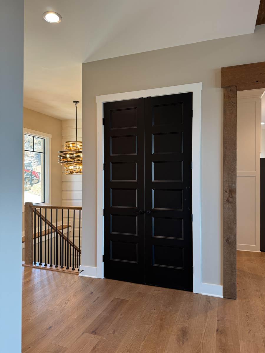 Interior view of a hallway with black double doors, a staircase with black spindles, and a wood beam accent.