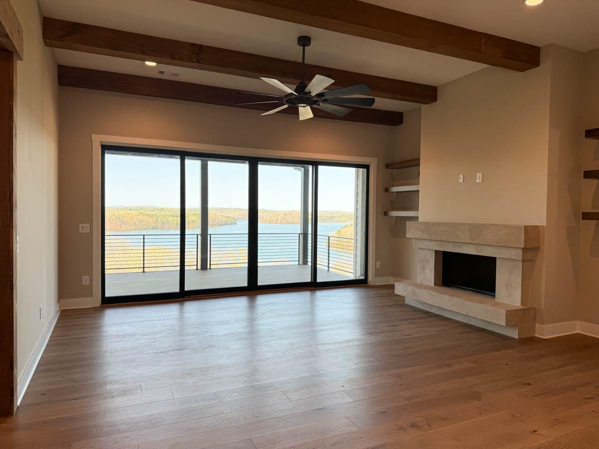 Interior view of great room with vaulted ceiling, exposed beams, fireplace, and large sliding glass doors overlooking a body of water.