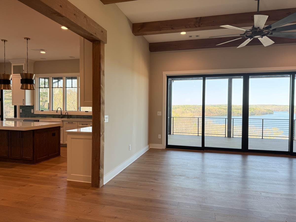Open concept living area and kitchen with wood beams, island, and sliding glass doors to deck with lake view.