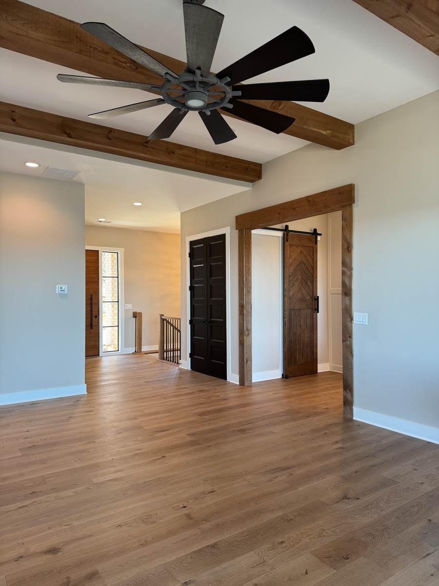 Interior view showing wood floors, exposed wood beams on ceiling, large fan, and double barn doors.