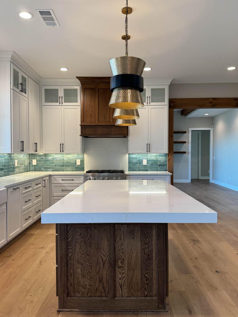 Kitchen with island, white cabinets, wood range hood, teal backsplash, pendant lights, and wood beams.