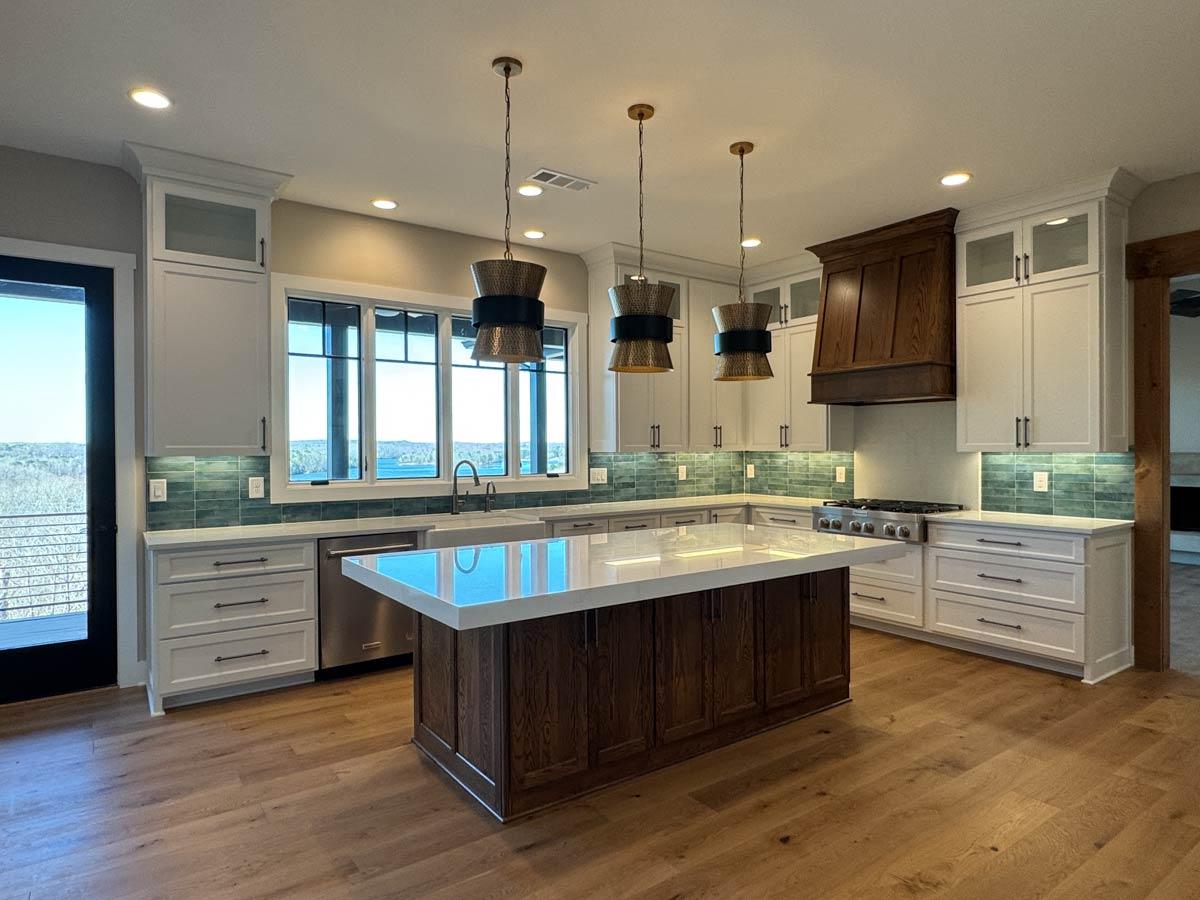 Kitchen featuring white shaker cabinets, a dark wood island with quartz countertop, stainless steel appliances, and a large window overlooking a lake.
