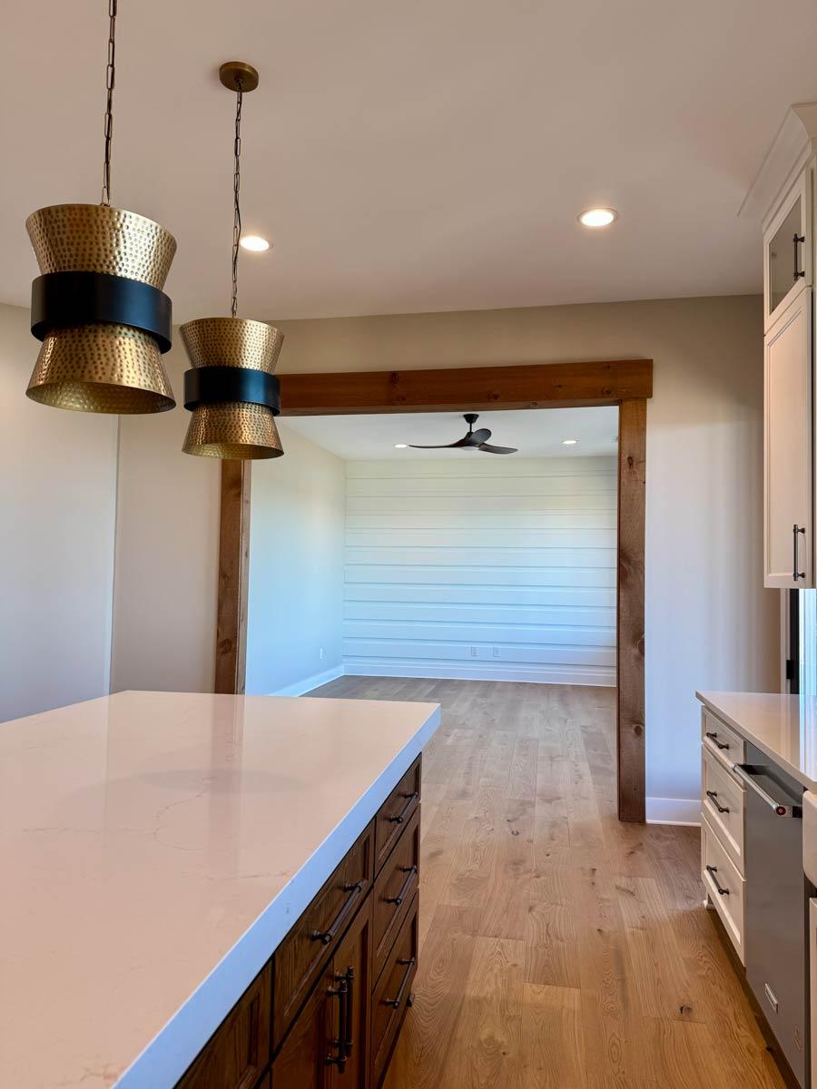 Kitchen island with quartz countertop and wood cabinets, open doorway to dining area with shiplap wall and ceiling fan.
