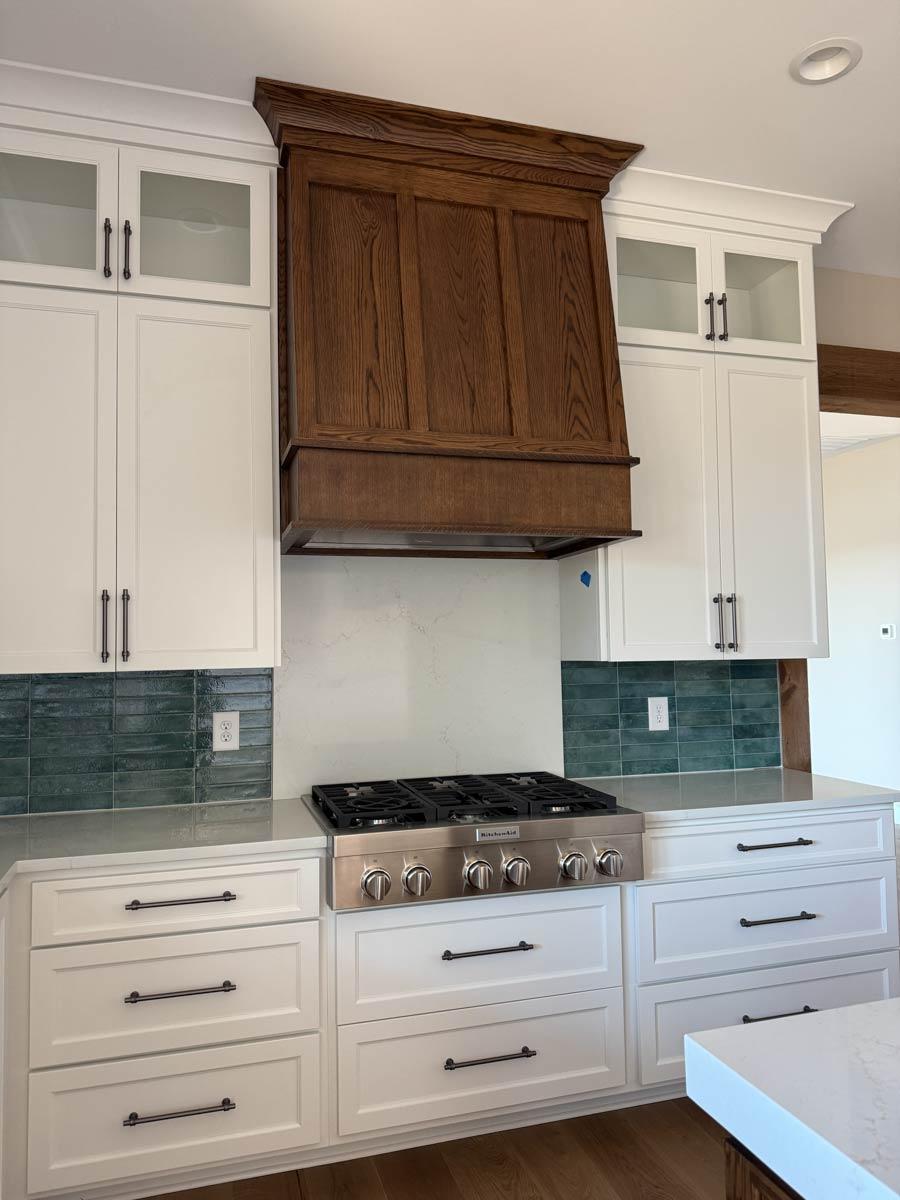 Kitchen with white cabinets, stainless steel range, and wood range hood with inset paneling. Teal subway tile backsplash.
