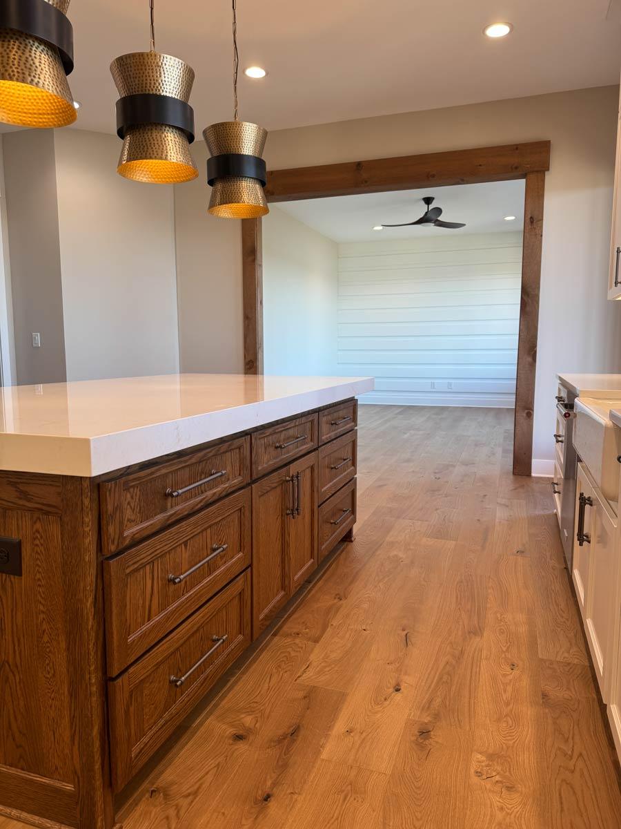 Kitchen with wood island, quartz countertop, and farmhouse sink, opening to a sunroom with shiplap walls and ceiling fan.