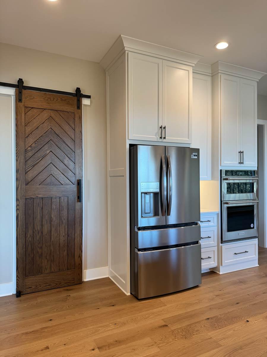 Kitchen with stainless steel refrigerator, built-in oven, and chevron barn door with black hardware.