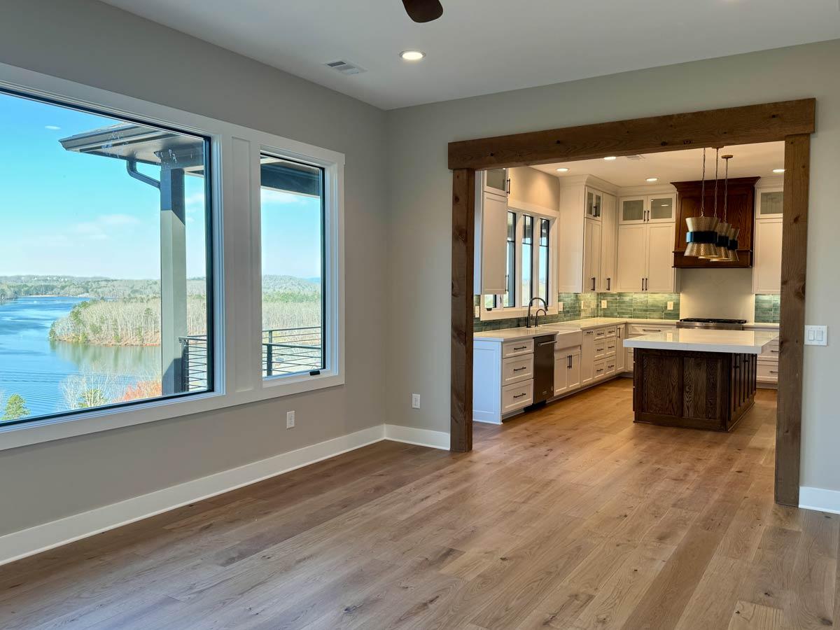 Interior view of open-concept living space with large windows overlooking water and a modern kitchen with island.