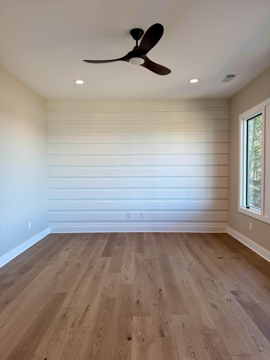 Interior view of a room with shiplap accent wall, hardwood floors, modern ceiling fan, and recessed lighting.