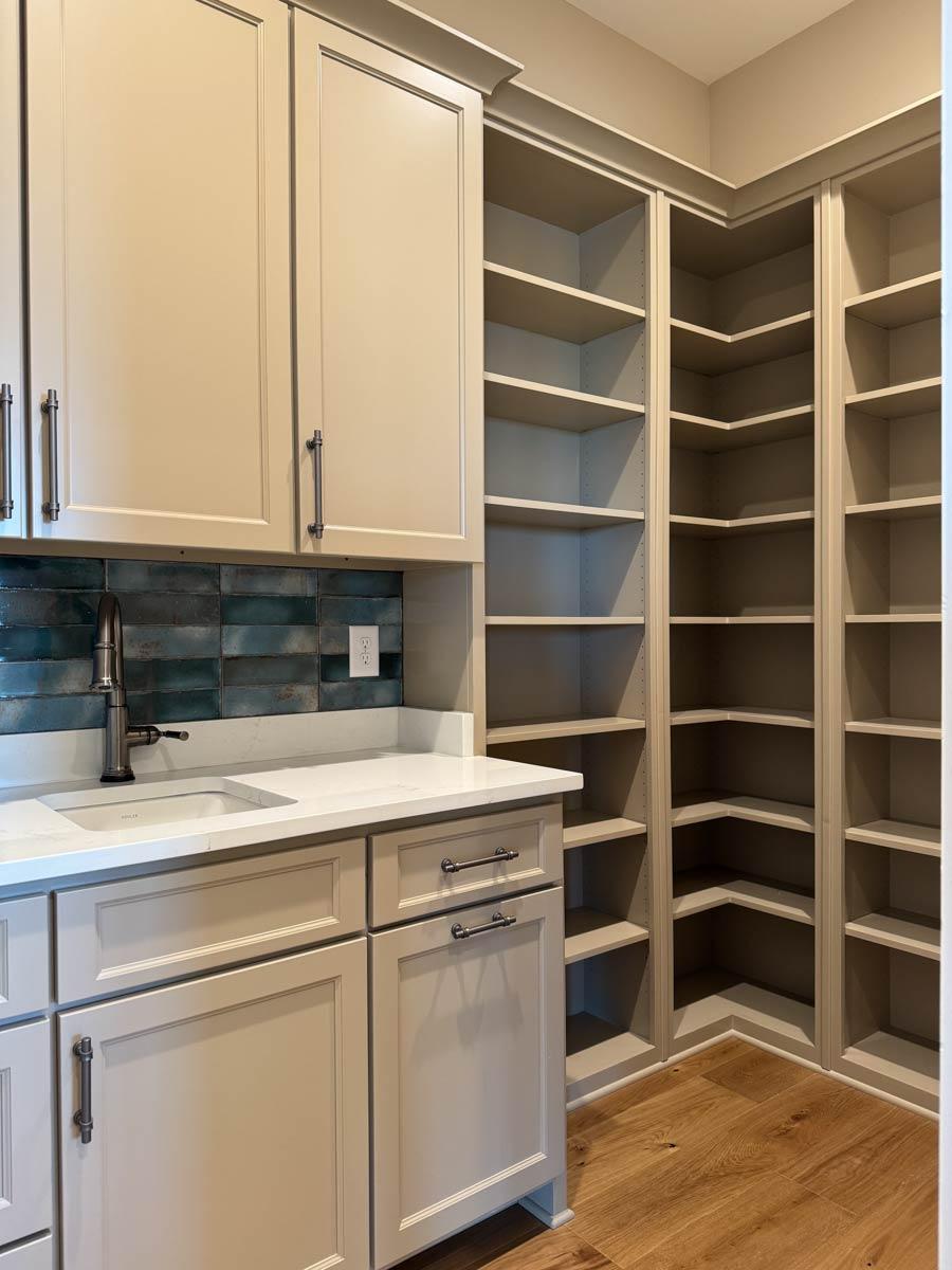Pantry interior with extensive shelving, light gray cabinets, quartz countertop, and subway tile backsplash.