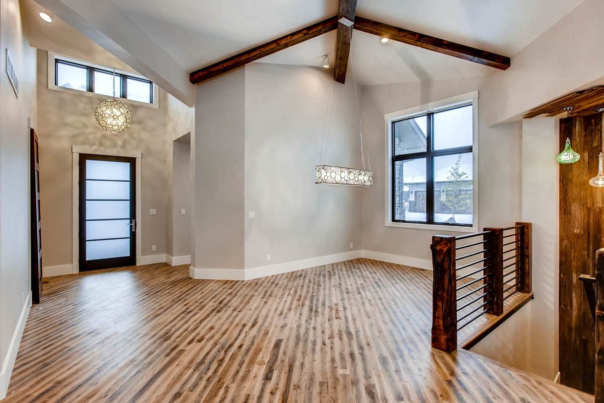 Interior view of open living space with vaulted ceilings, exposed wooden beams, modern door, and large windows.
