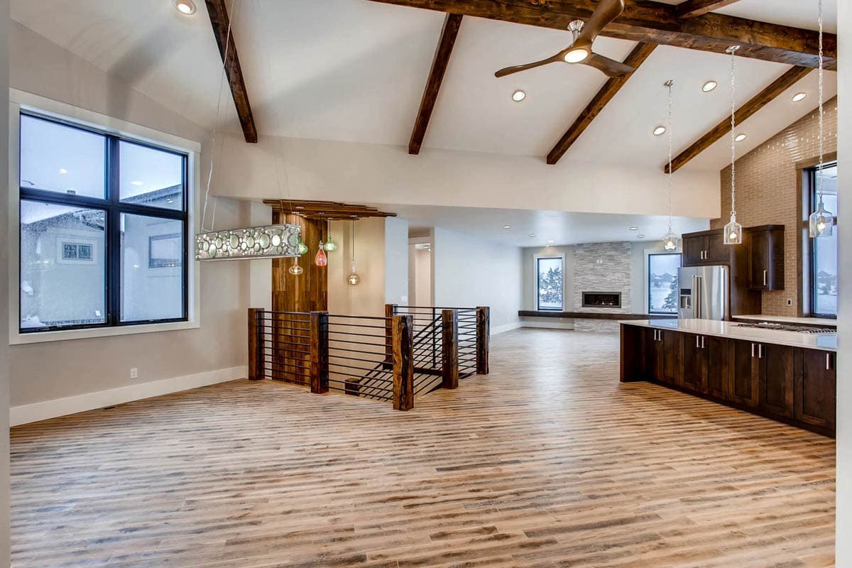 Interior view of open concept living space with vaulted beamed ceiling, fireplace, kitchen island, and large windows.