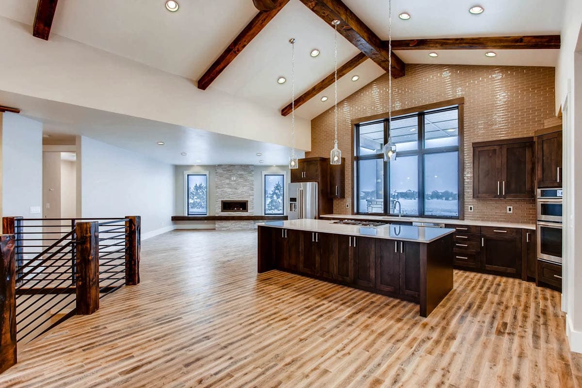 Great room and kitchen with vaulted ceilings, exposed beams, island, stone fireplace, and large windows.