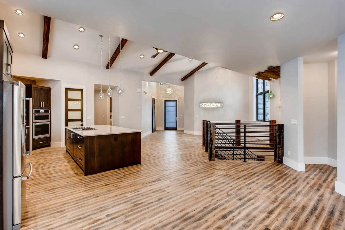 Interior view of open-concept living area with vaulted ceiling, exposed beams, kitchen island, and staircase.