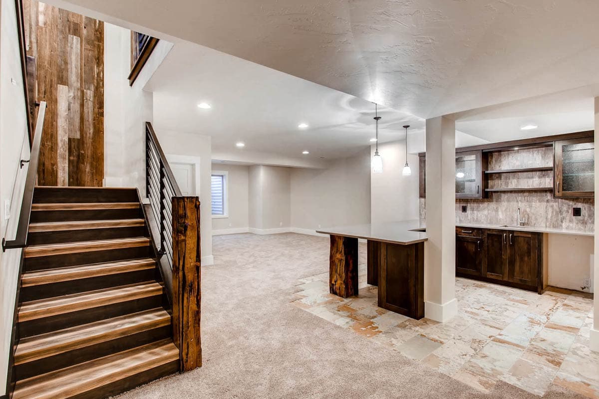 Basement interior with wood-paneled staircase, open living area, and wet bar with dark cabinetry and island.