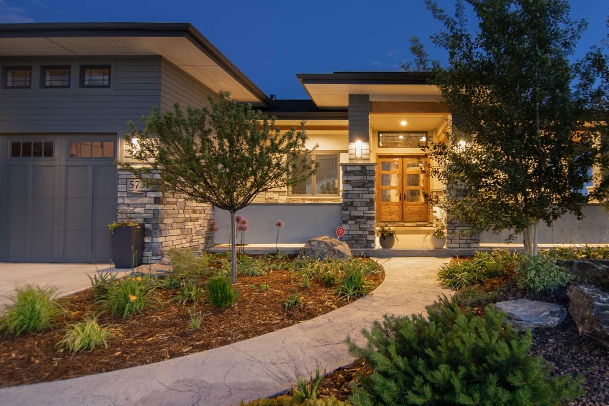 House plan exterior: Modern home with wide eaves, stone accents, double wooden entry doors, and attached garage.