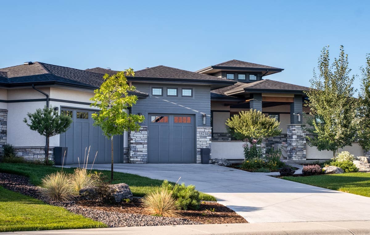 House plan exterior: Contemporary style with a prominent hip roof, stacked stone accents, and a three-car garage.