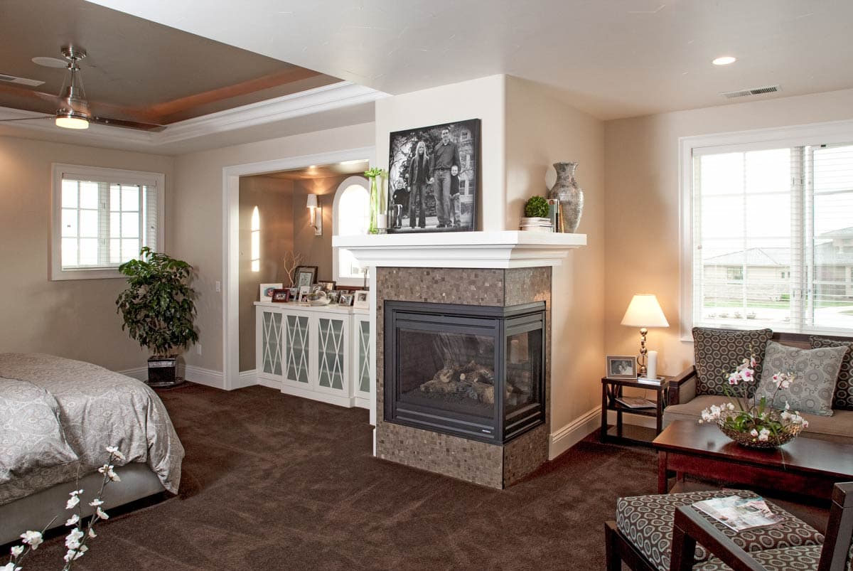 Interior view of bedroom with gas fireplace, decorative cabinet, and ceiling fan.