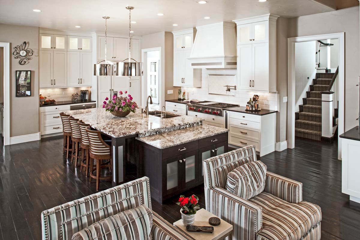 Spacious kitchen with large island, white cabinets, granite countertops, professional range, and adjoining staircase.