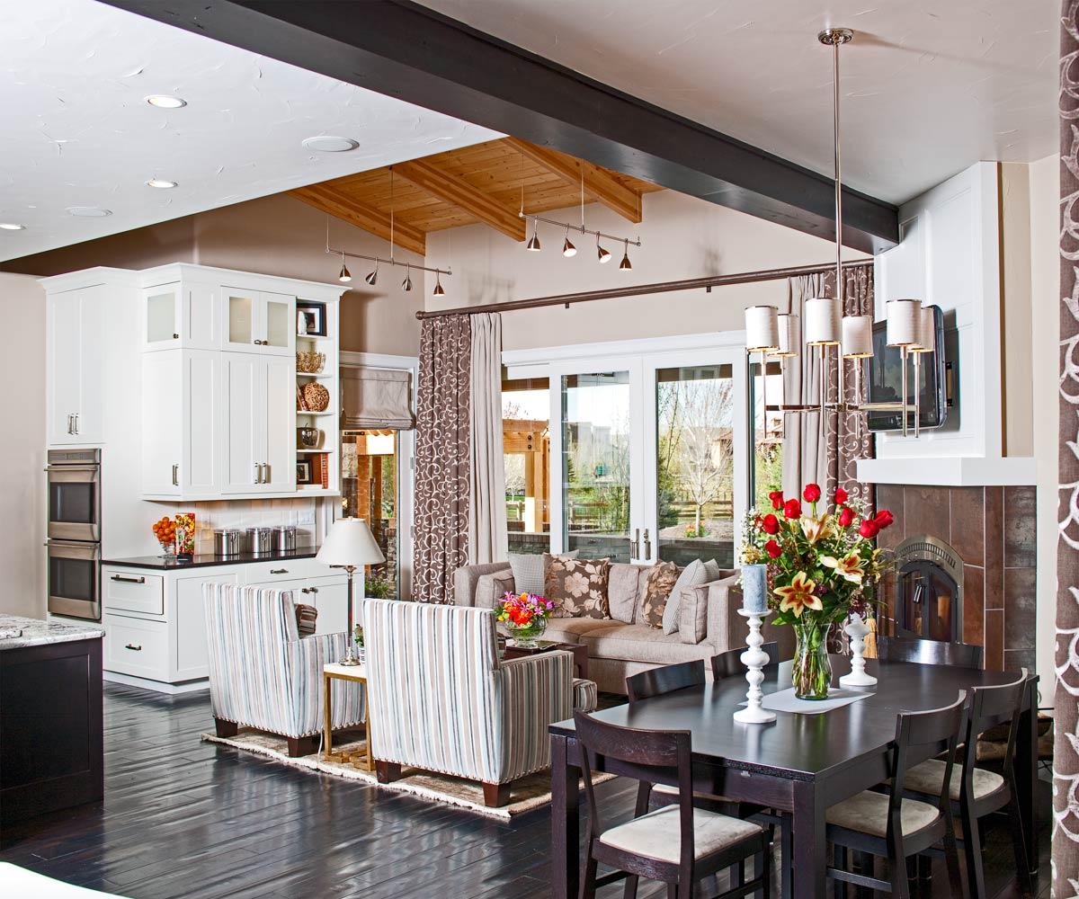 Open concept living area with white kitchen cabinetry, dining table, fireplace, and vaulted wood-beamed ceiling.