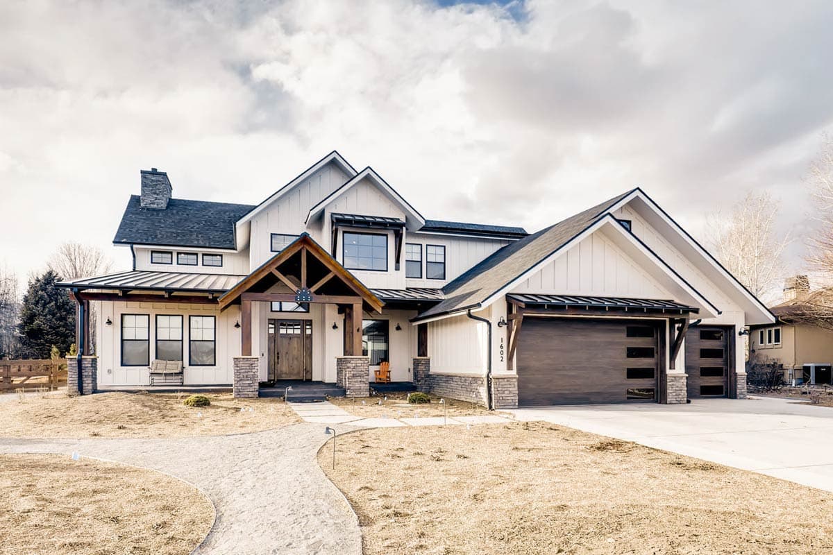 House plan exterior. Modern Farmhouse style, two-story home with a gabled roofline, front porch with exposed timber supports, and attached garage.