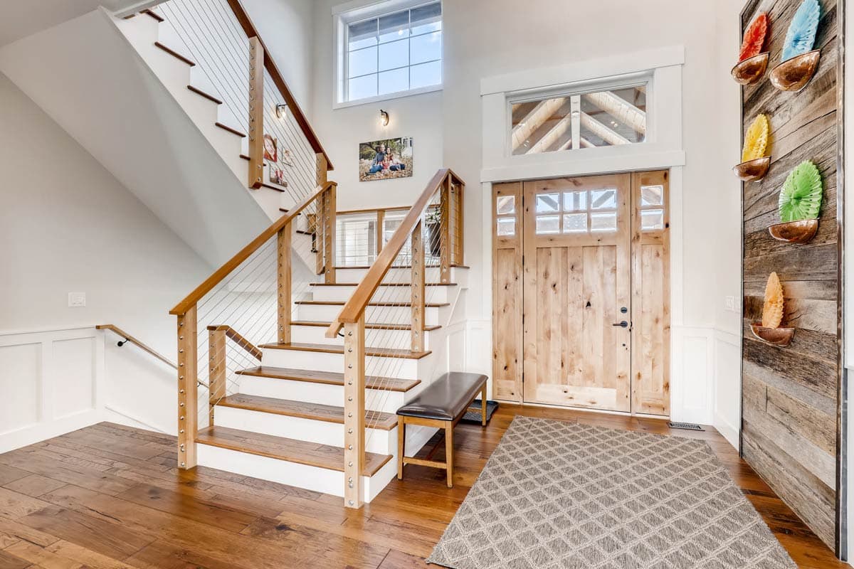 Interior view of entryway with wood flooring, a wooden staircase with cable railing, and a large double wooden door.