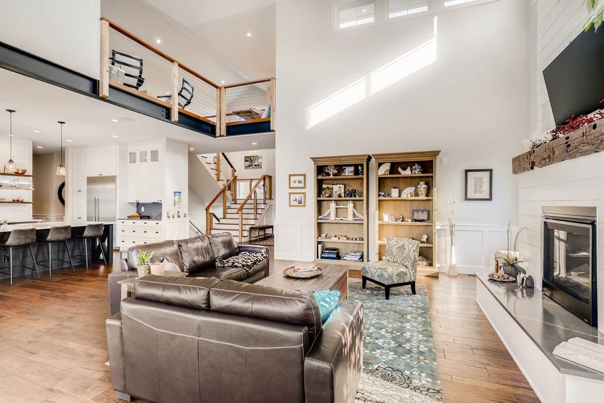Interior view of a great room with open loft, kitchen island, staircase, fireplace, and built-in bookshelves.