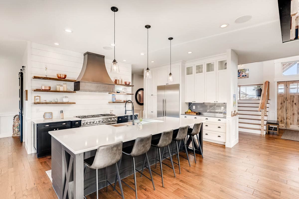Kitchen with large island, range with metal hood, and adjacent staircase with wooden doors.