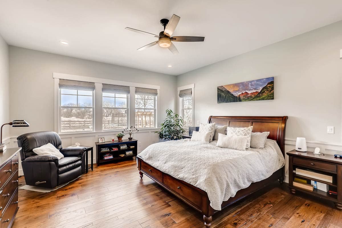 Bedroom with king-size bed, recliner, desk, and wall art above bed. Three large windows offer natural light.