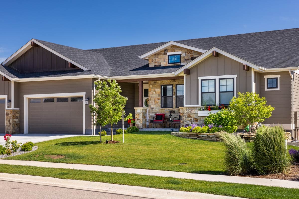 House plan exterior featuring a covered porch with stone accents, gabled dormers, and a two-car garage.