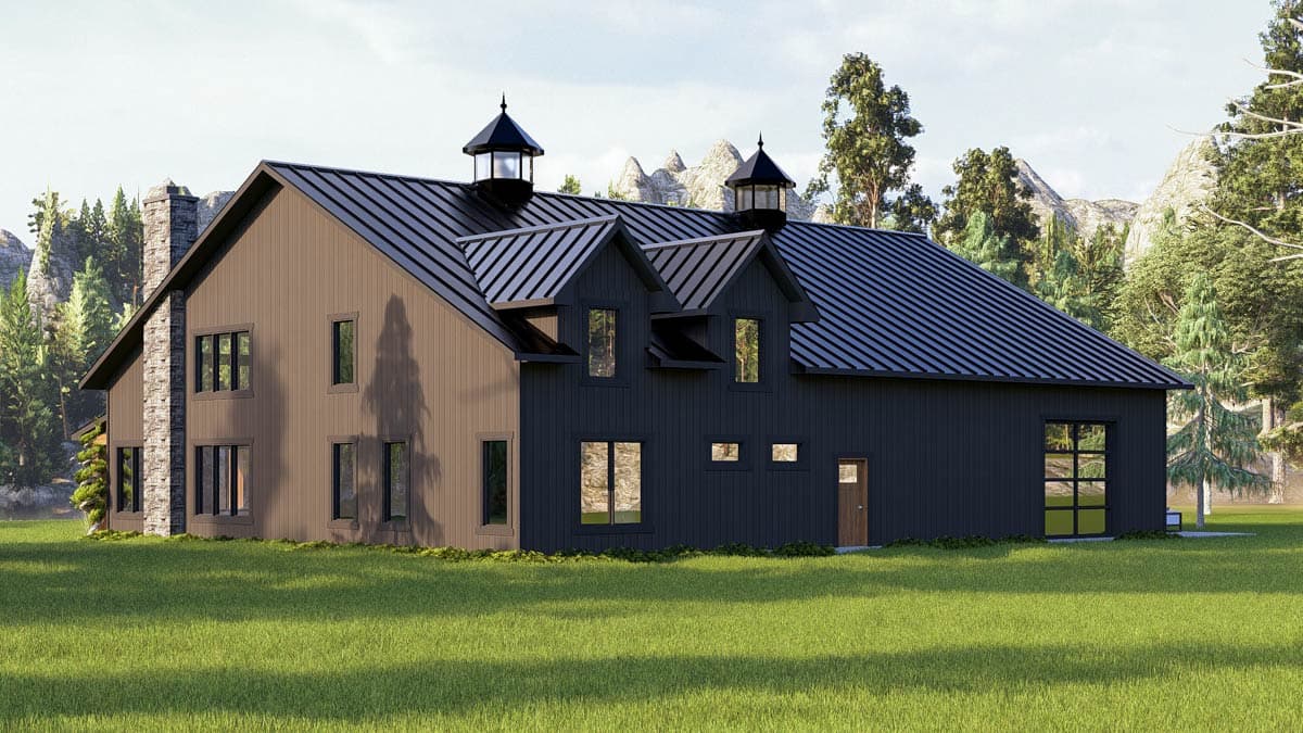 Modern two-story house with dark siding, a black metal roof, and stone chimney, set in a green field with mountain and forest background.