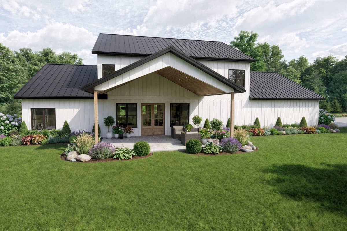 A modern farmhouse with a black roof and white siding, featuring a covered porch, manicured lawn, and lush landscaping.