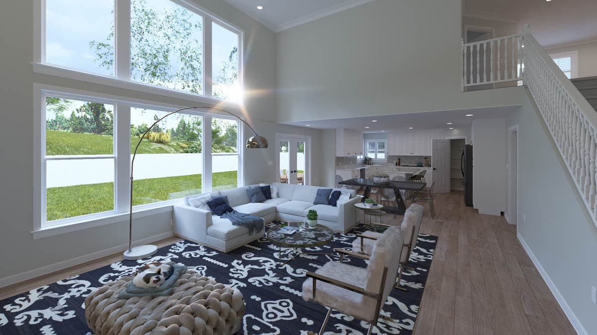 Living room with vaulted ceiling, large windows, open layout to kitchen, and staircase.