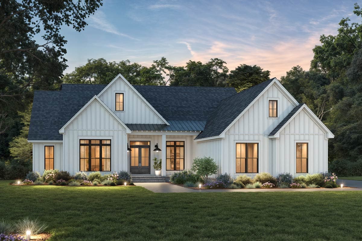 A white farmhouse with a dark roof and black window frames is framed by lush greenery. The front door is lit, and the sky is a soft blue.