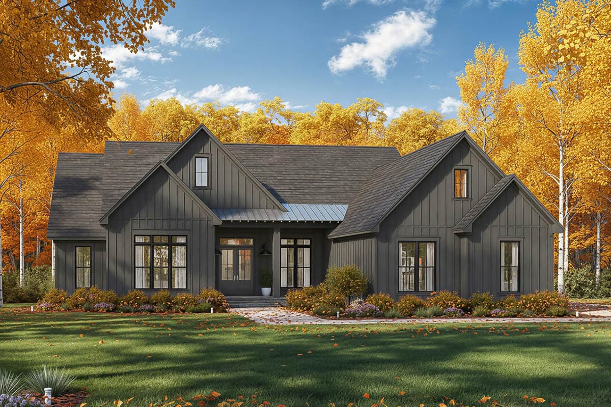 A modern farmhouse painted dark gray sits on a grassy lawn surrounded by fall foliage. The sky is blue with fluffy white clouds.