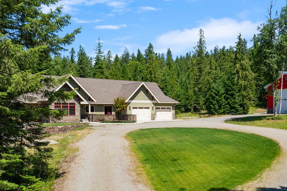 House plan exterior: Ranch style, light green siding, stone accents, gabled dormers, and a three-car garage.
