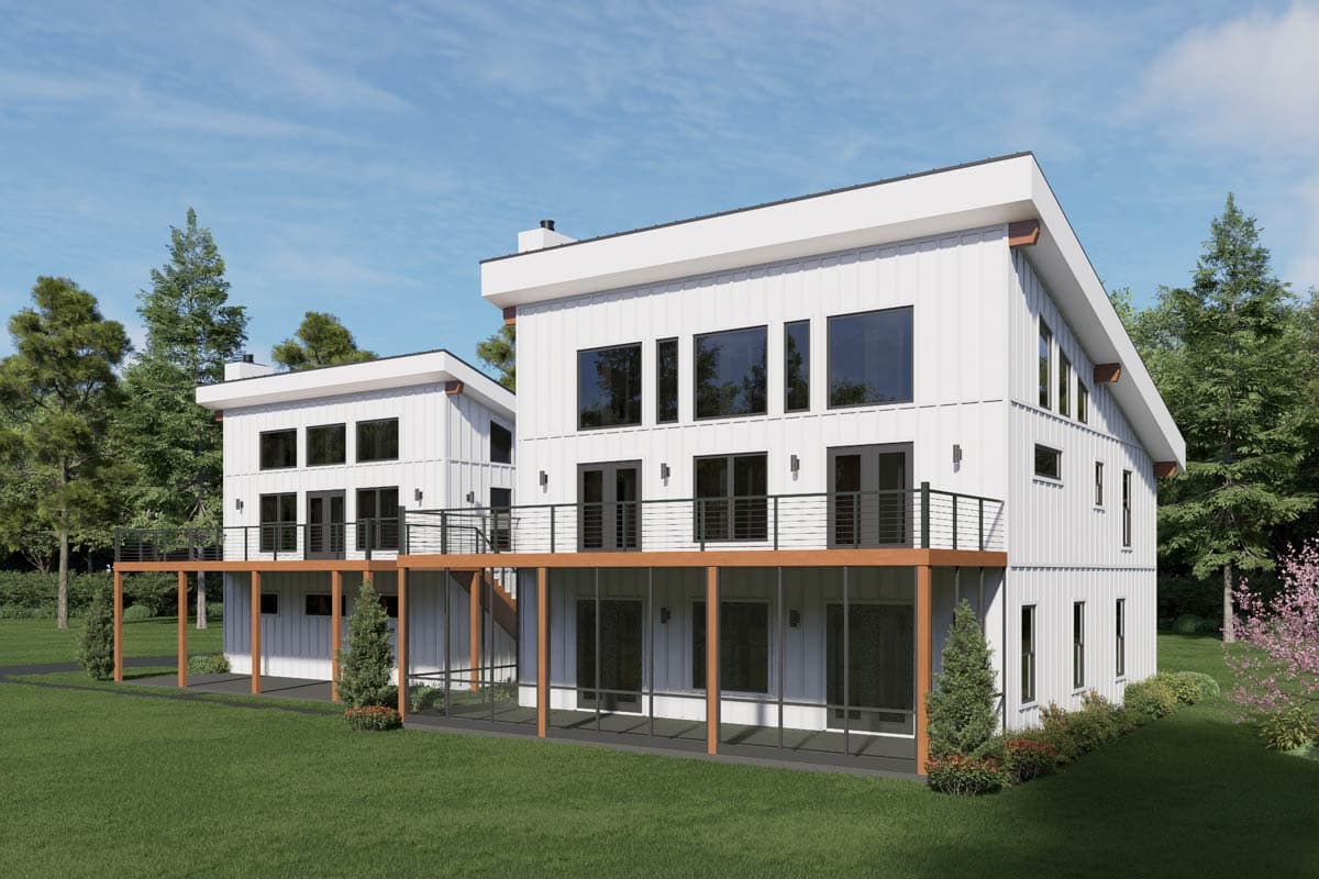 Modern two-story white house with large windows, balconies, and a wraparound deck, set on a grassy lawn with trees and a blue sky.