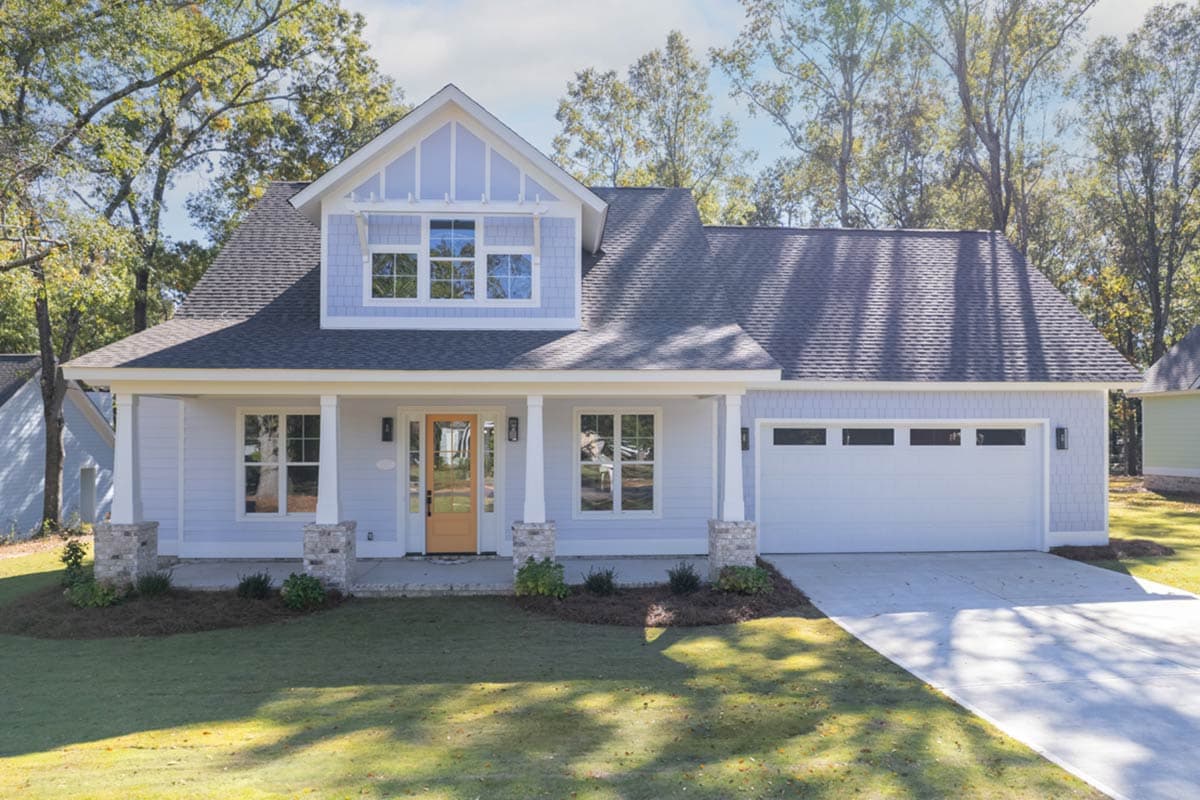 A two-story house with light blue siding, white trim, and a welcoming front porch, a pale orange door, and a white garage door.