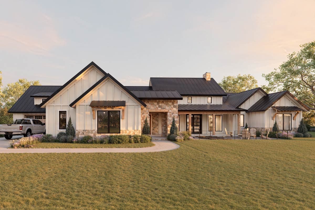A modern farmhouse with a dark roof and white siding is set on a lush green lawn. Stone accents and large windows are featured.